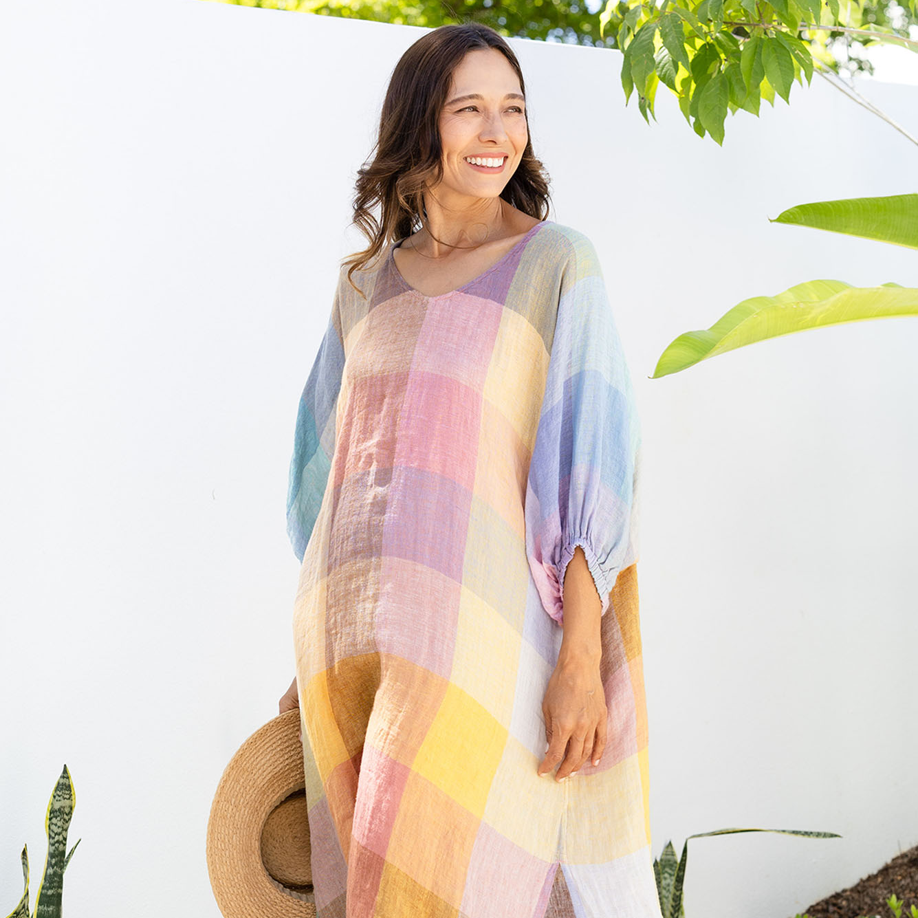 Brunette woman wearing a colourful checkered dress in a garden.