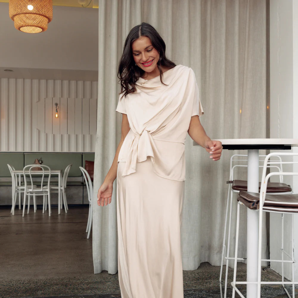 Brunette woman wearing a cream draping black tie set in a restaurant.