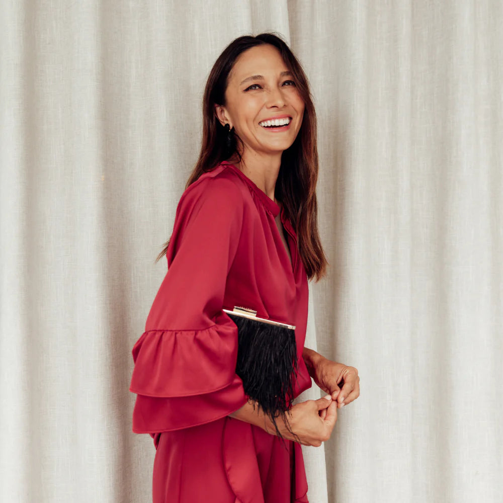 Brunette woman wearing a red silk black tie set in front of white curtains.