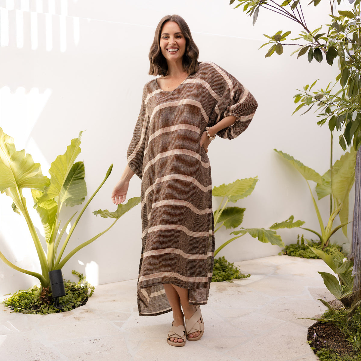Brunette woman in a brown and beige stripe long open-weave kaftan dress.