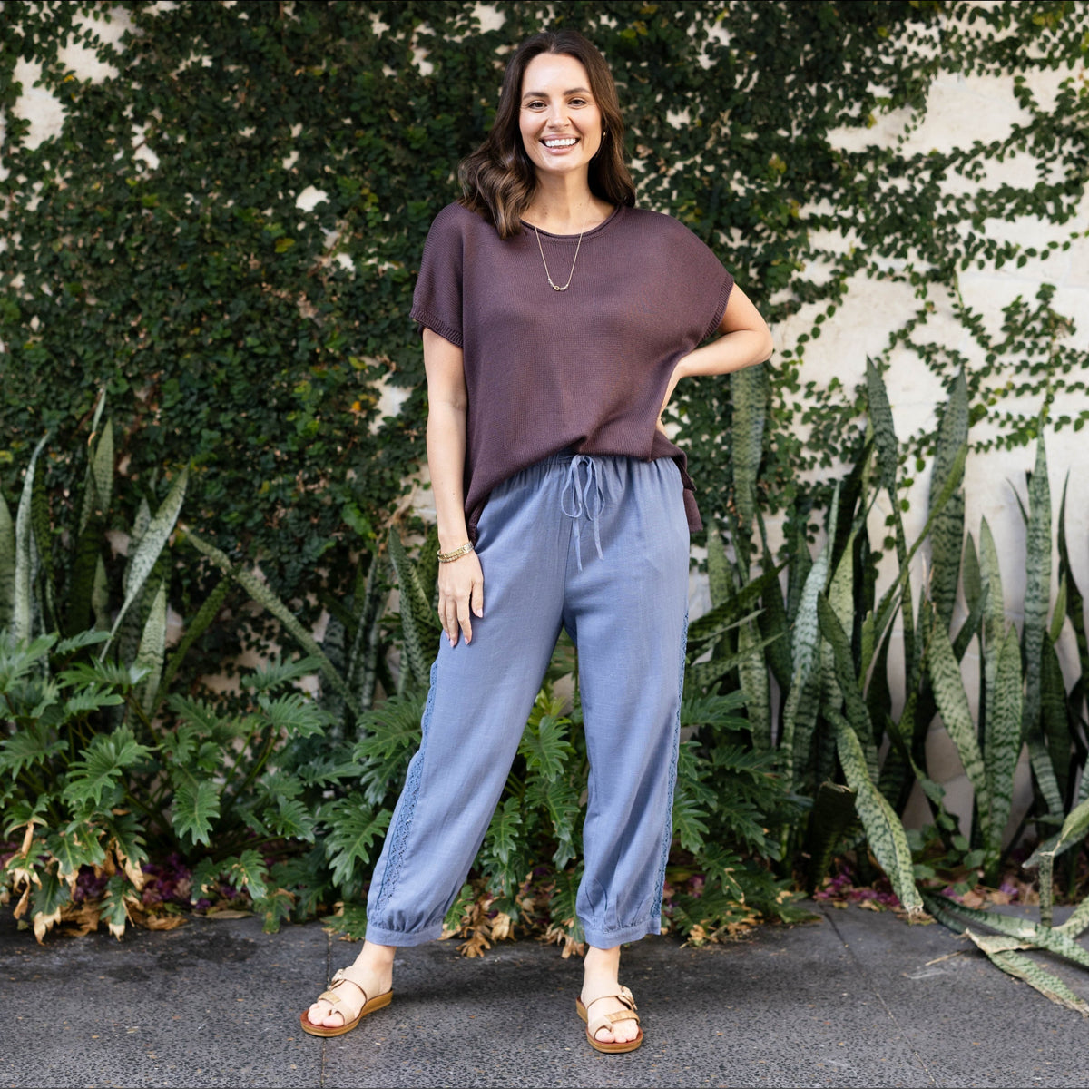 Brunette woman wearing blue linen pants and a brown top.
