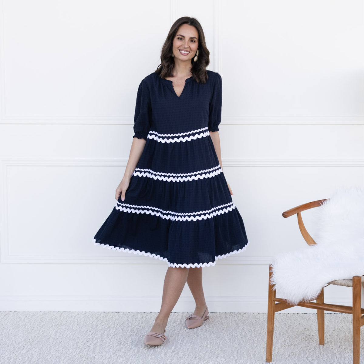 Brunette woman stands wearing a contrast panel dress with sleeves and a full skirt to the knee, suitable for petites.
