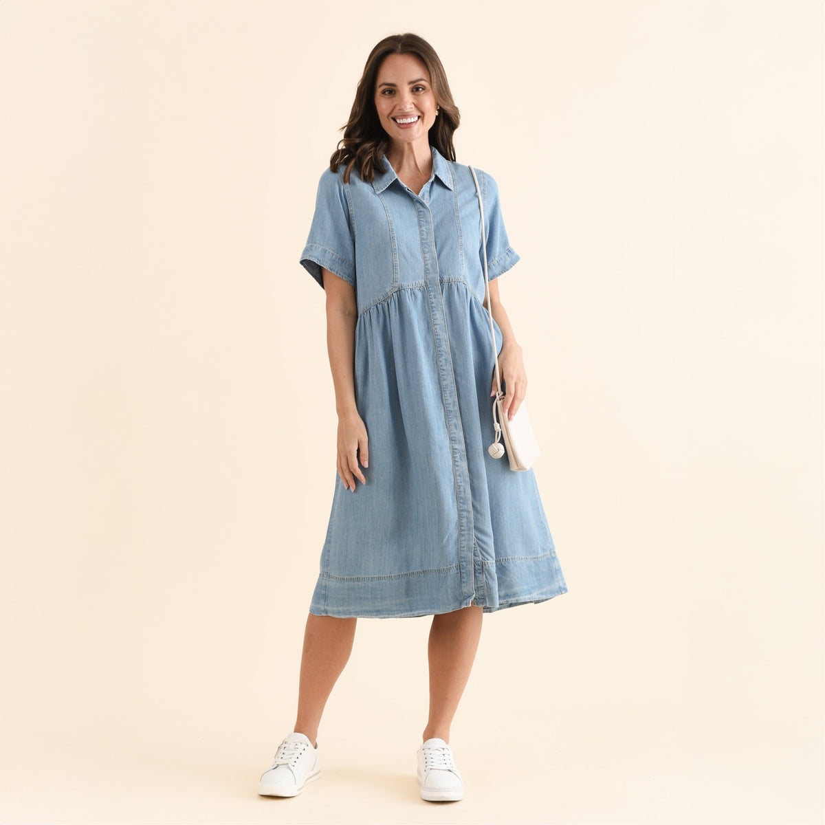 Brunette woman in a denim dress with a crescent waistline and collar that falls below the knee