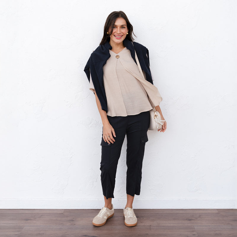 Brunette woman wearing black cargo pants and a tan top with a black sweater