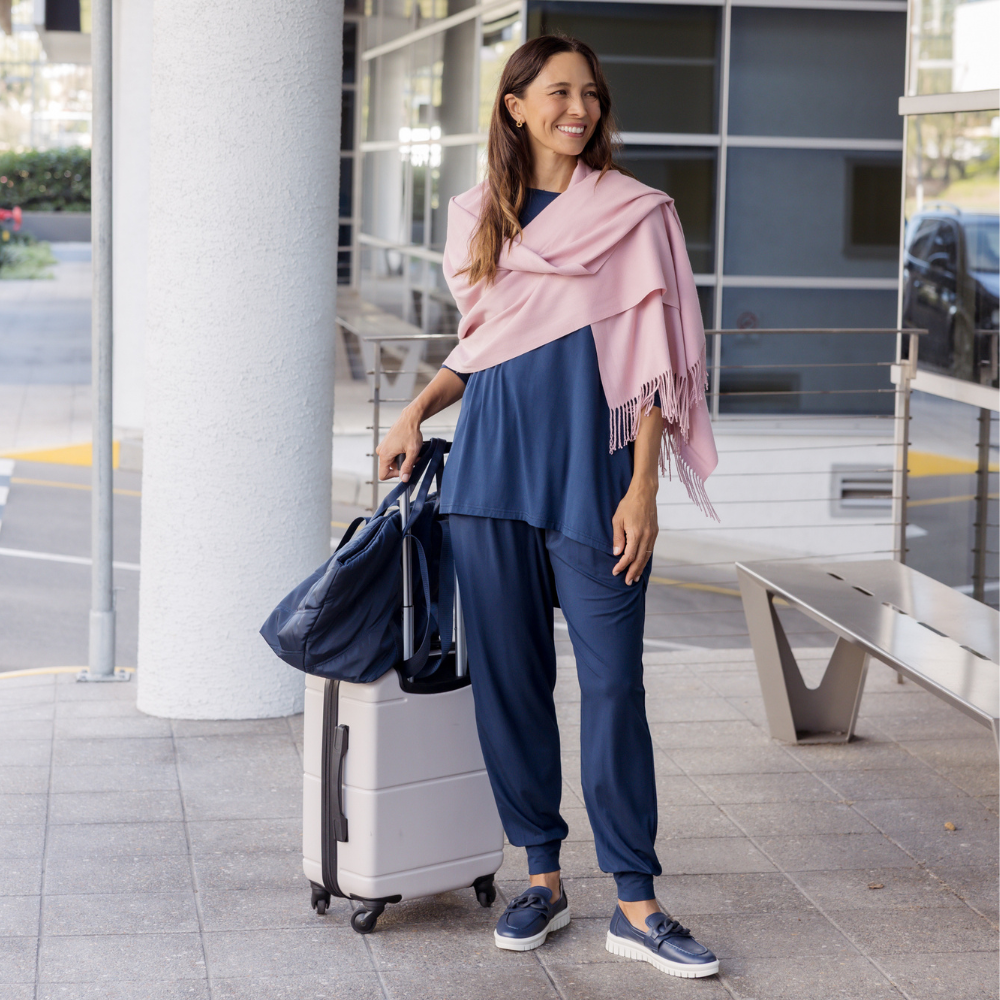 Brunette model wearing a navy travel outfit holding a suitcase.
