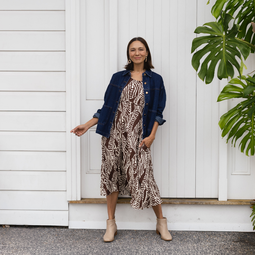 Brunette woman wearing a relaxed brown midi dress with a denim jacket and beige ankle boots.