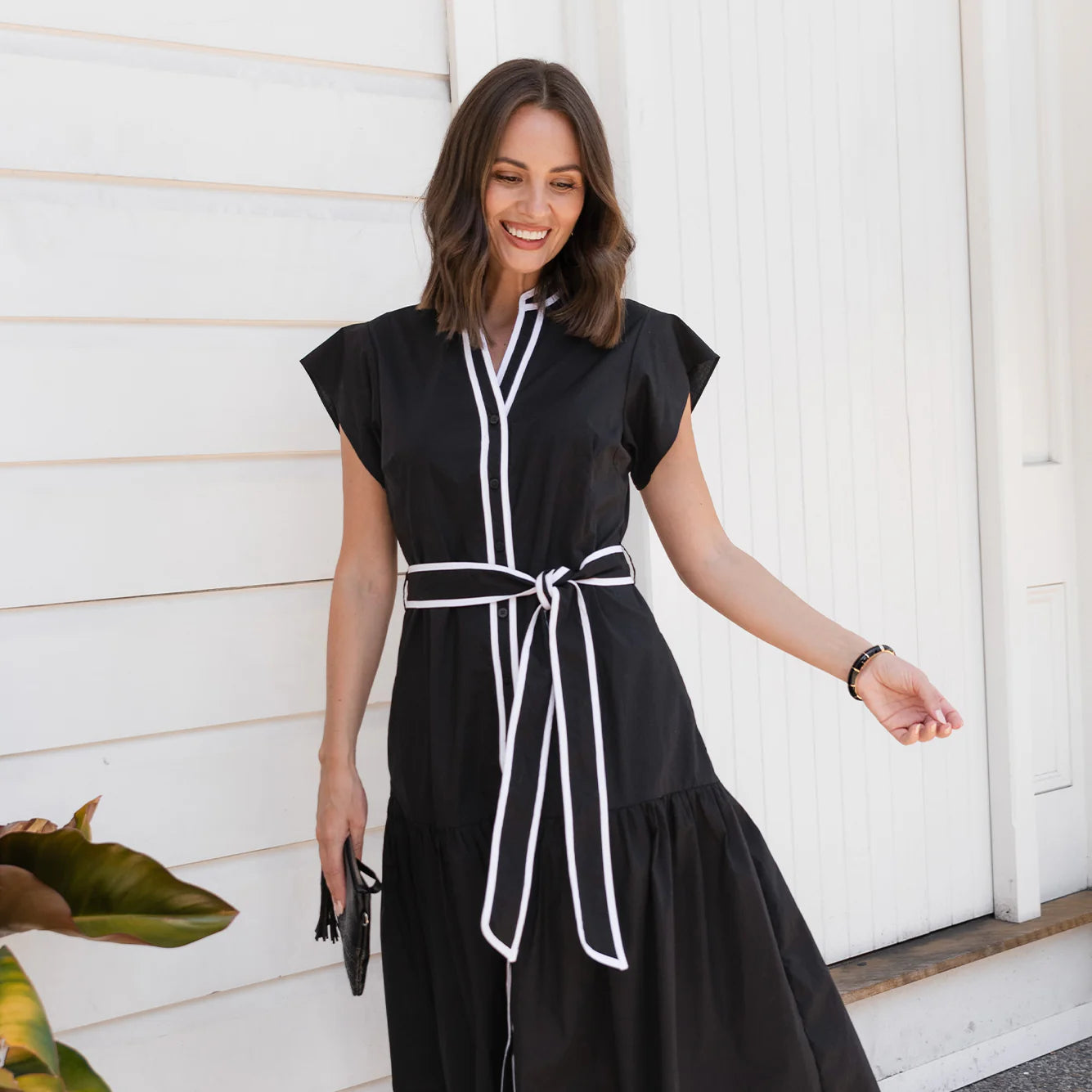 Brunette woman wearing a black cocktail dress in front of a white wall.