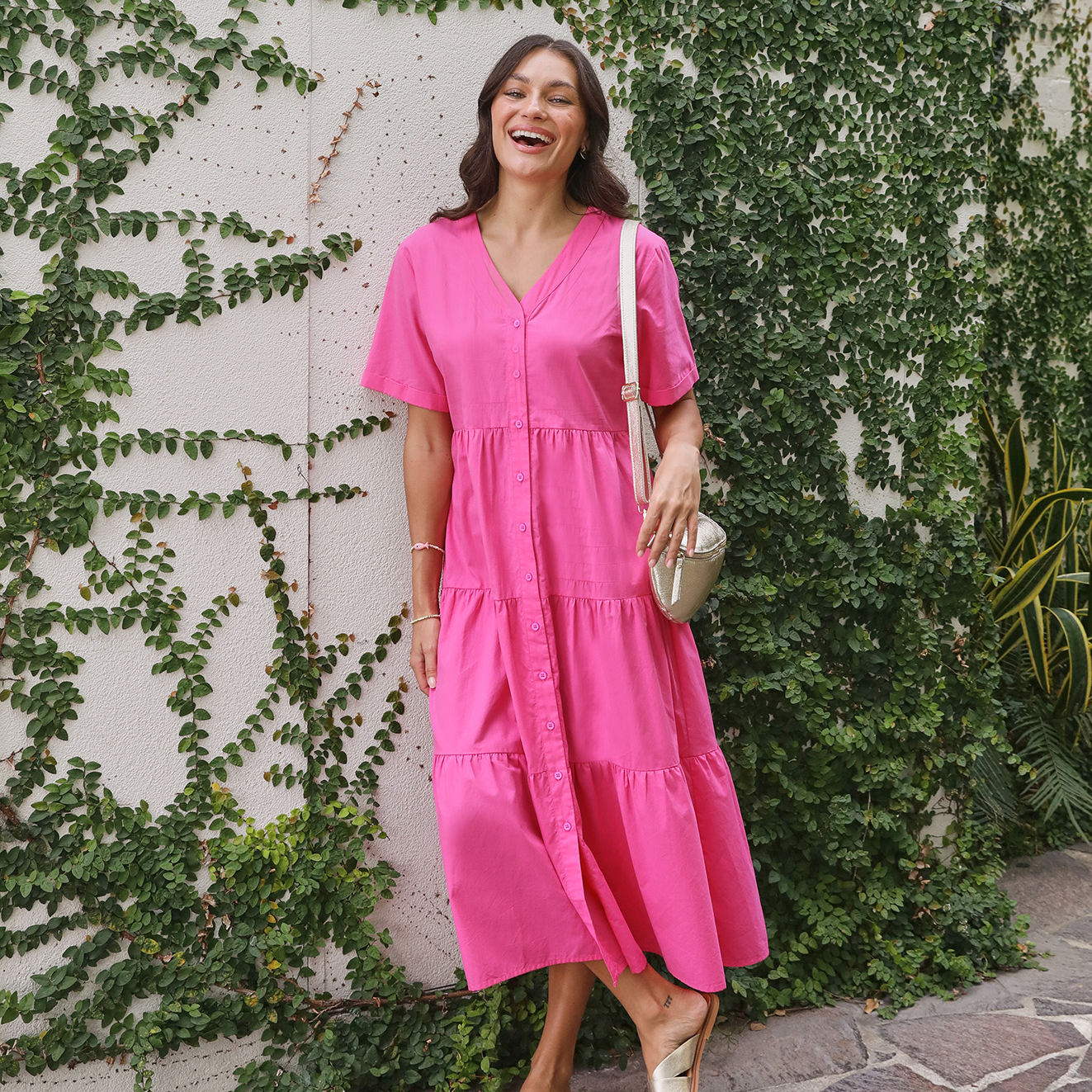 Brunette woman in a hot pink tiered dress holding a gold bag.
