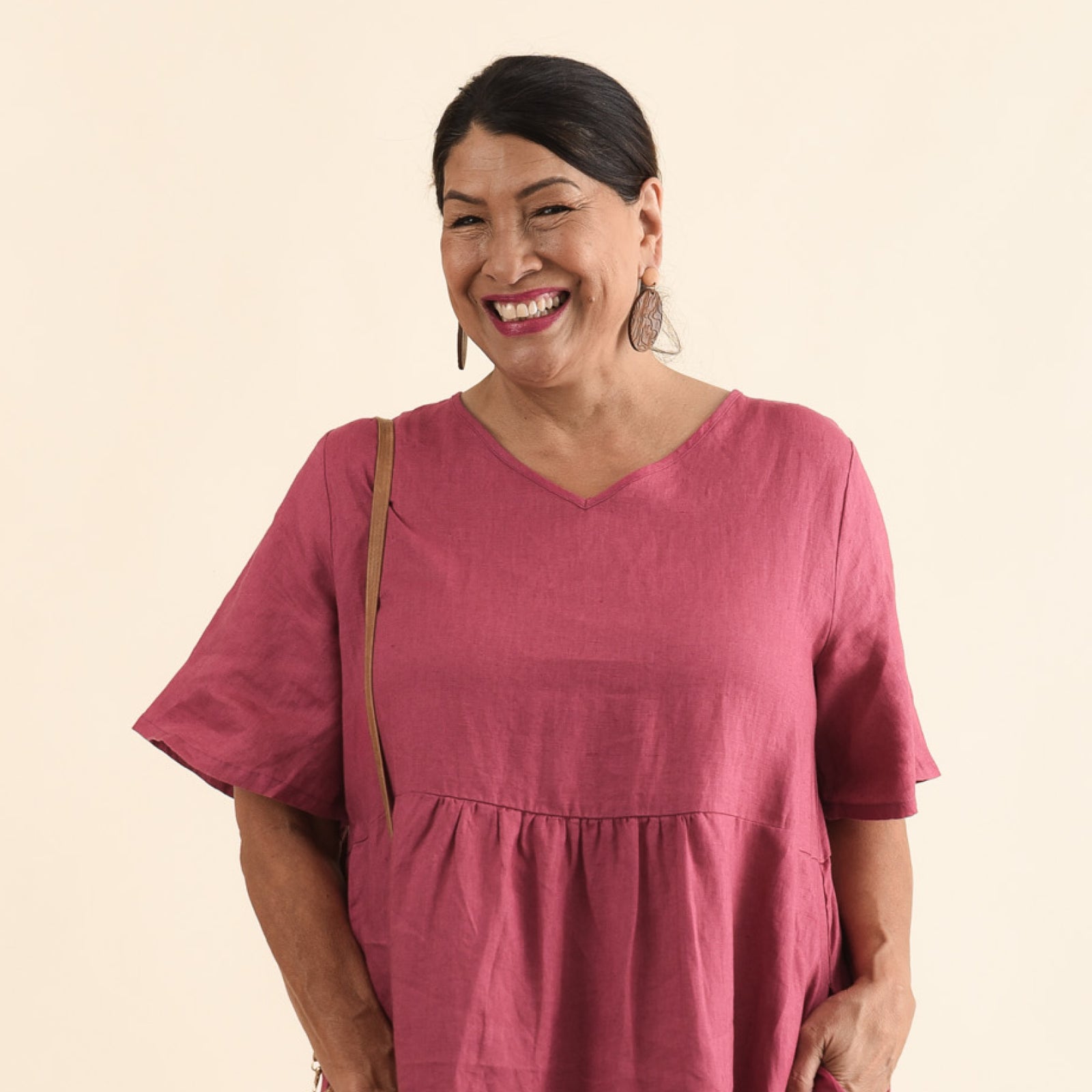 Brunette woman wearing a pink linen midi dress with half sleeves and a V-neckline, and brown disc earrings.
