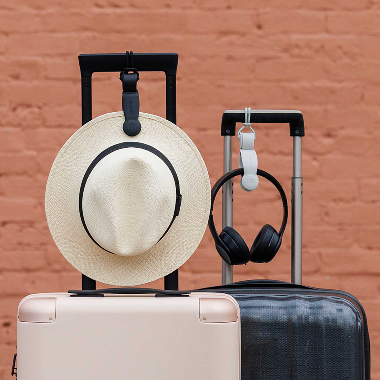 Wide-brim hat and black headphones attached to suitcases with a Klipsta hat clips.