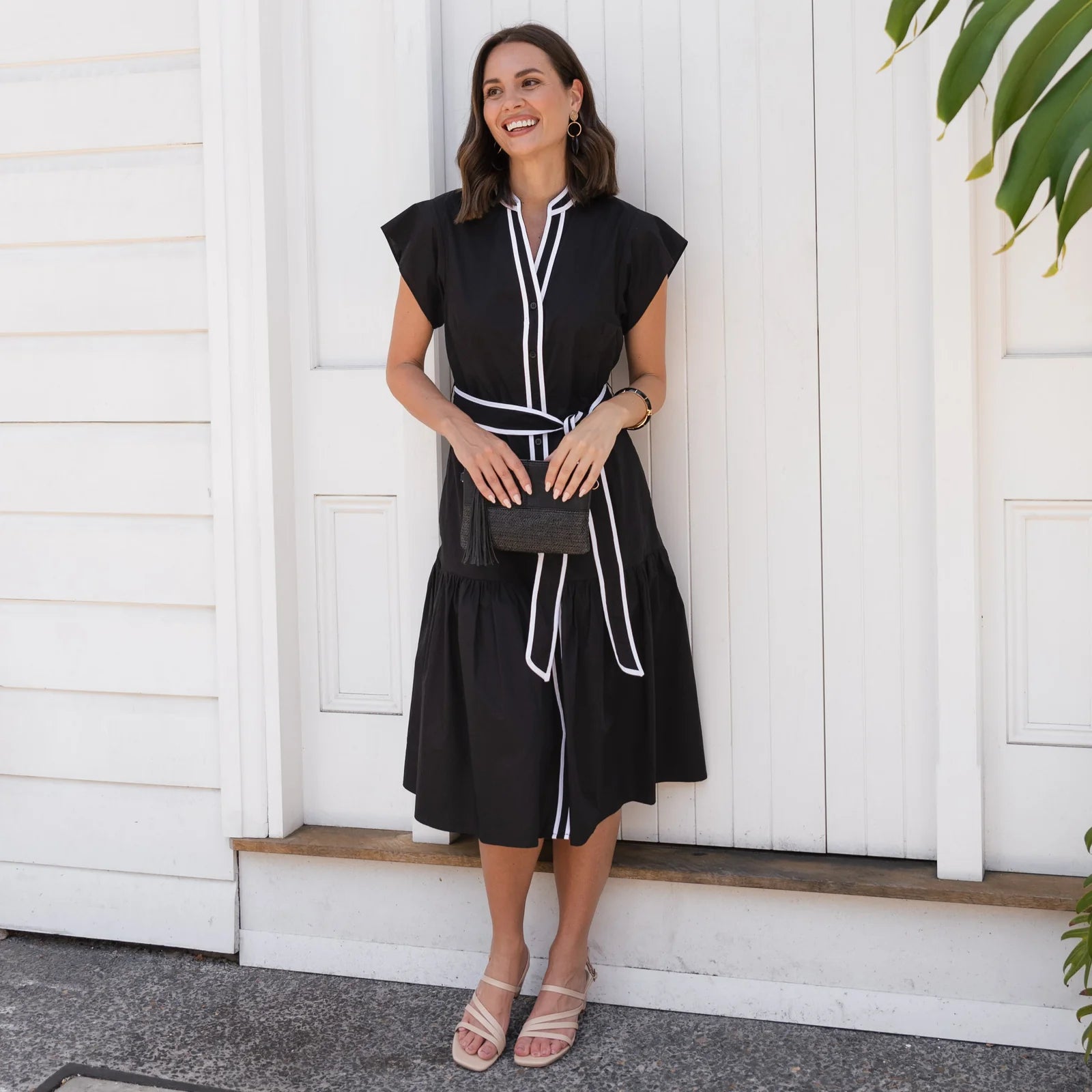 Brunette woman wearing a black midi dress in front of a white wall.