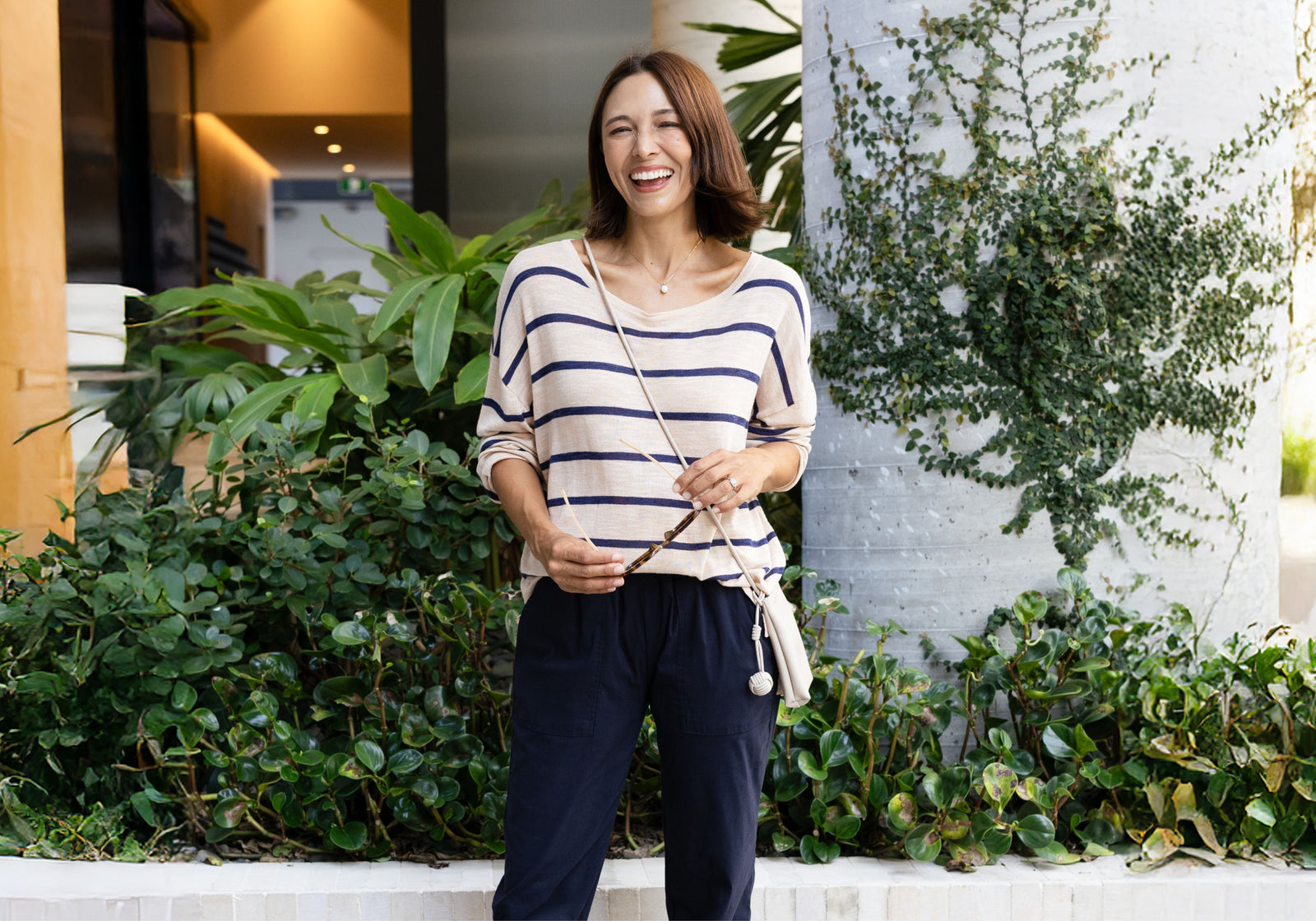 Brunette woman smiling in a comfortable stretchy travel outfit in neutral colours looks ready to go. 