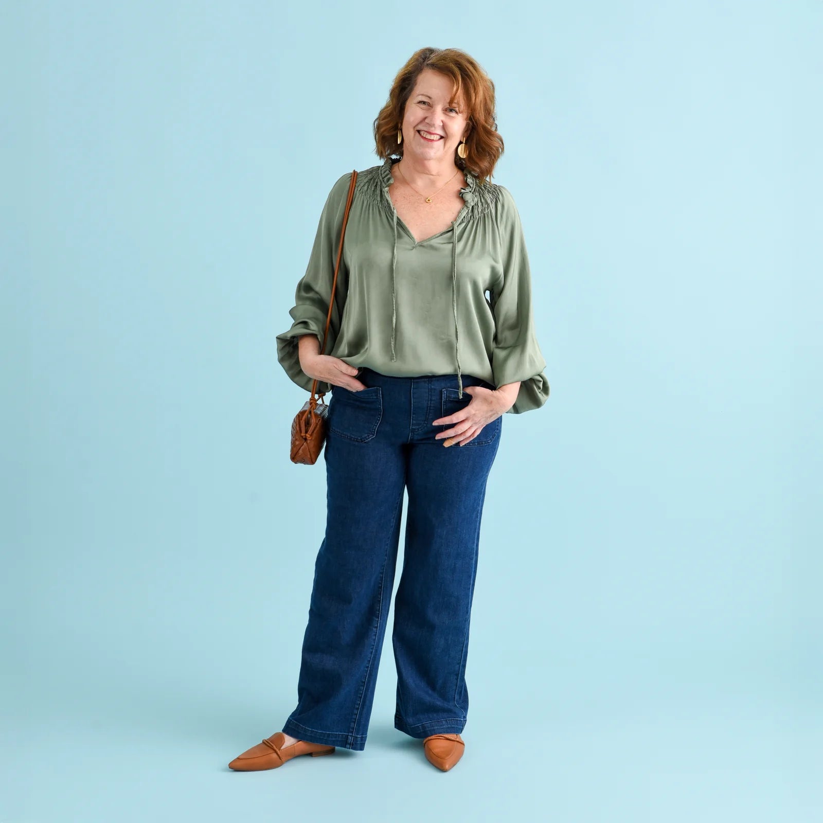 Brunette woman wearing blue denim jeans and a sage green blouse.