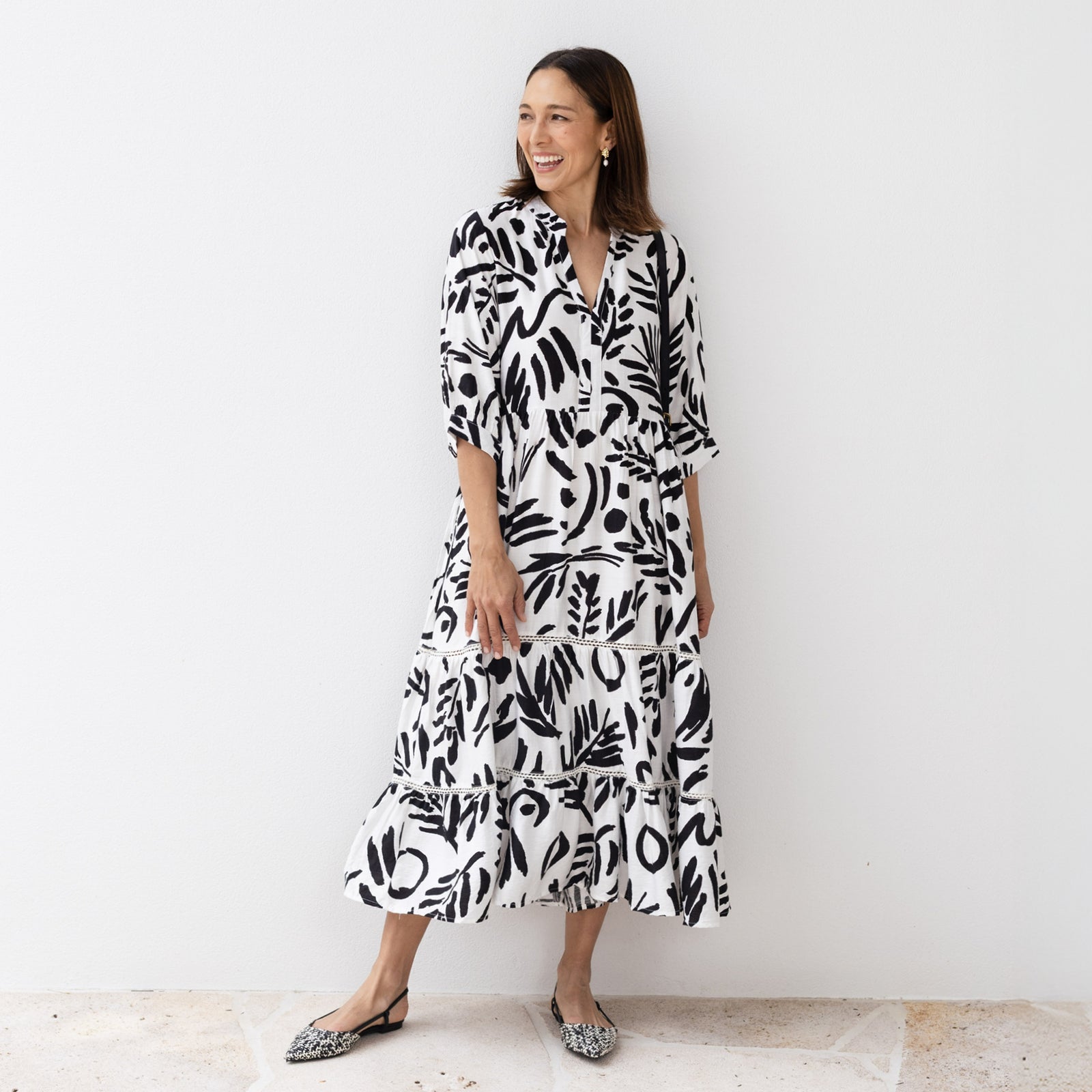 Brunette woman standing in a monochrome midi dress and pointed flat pumps looking event-ready.
