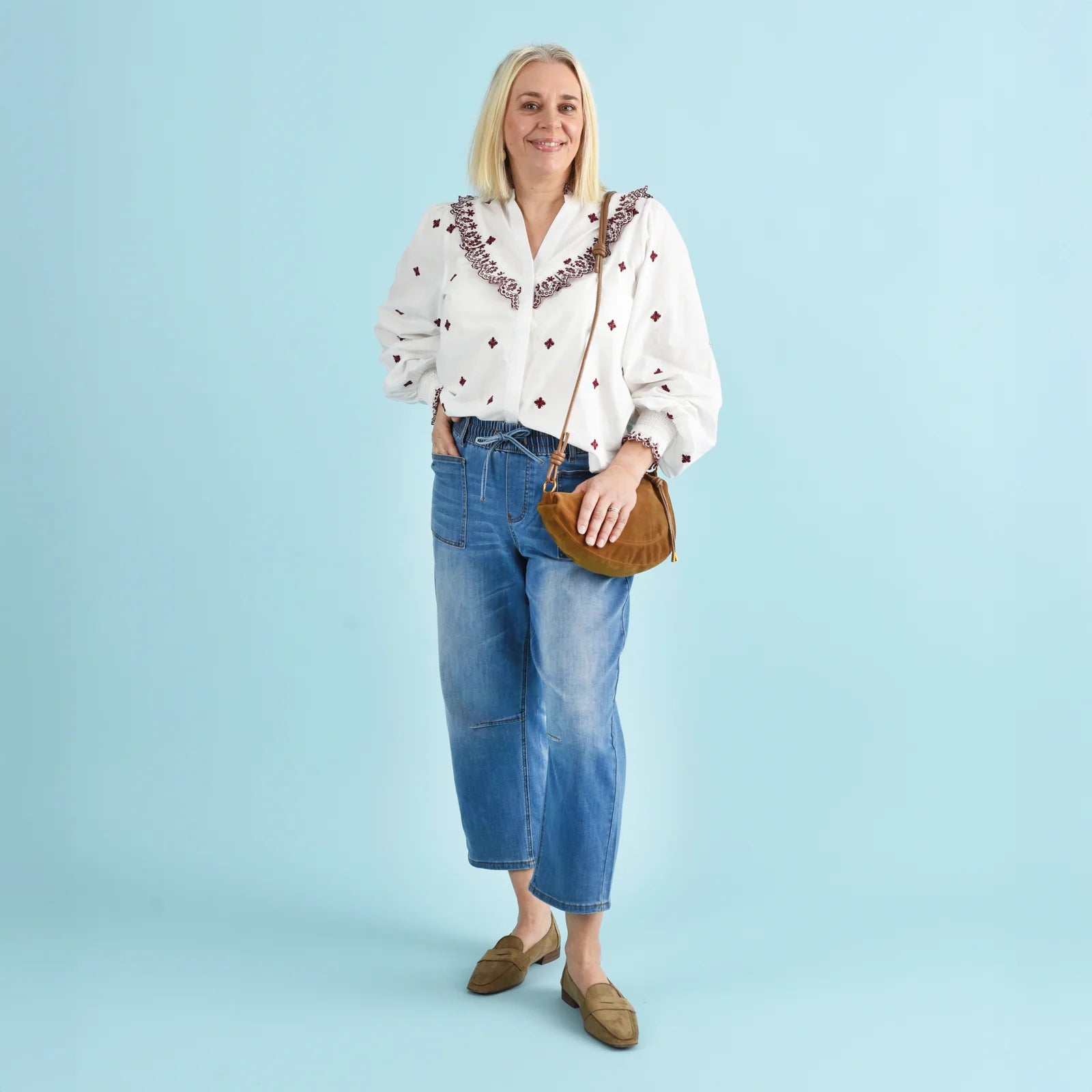 Blonde woman wearing blue denim jeans and a white and red blouse.