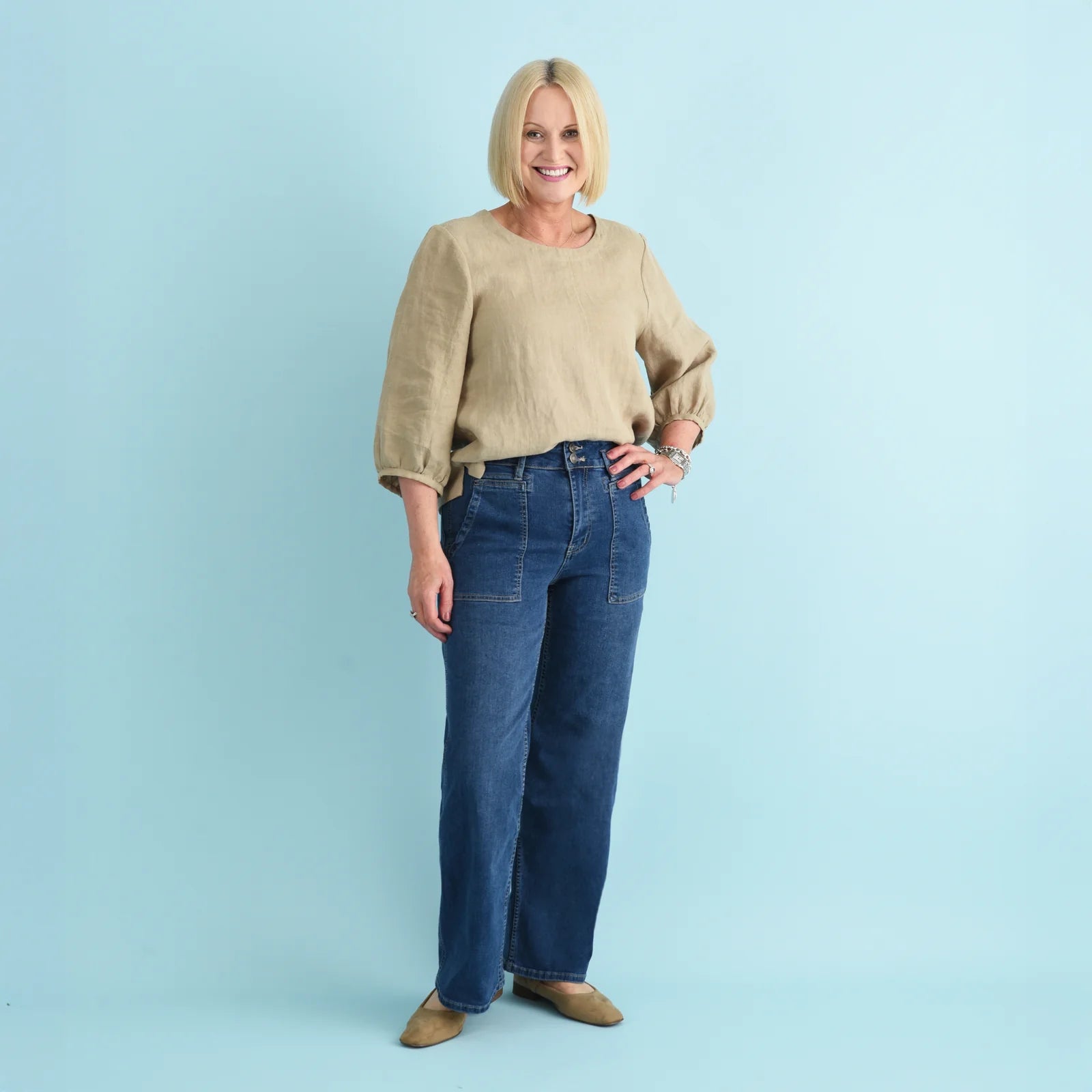 Blonde woman wearing blue denim jeans and a beige linen top.