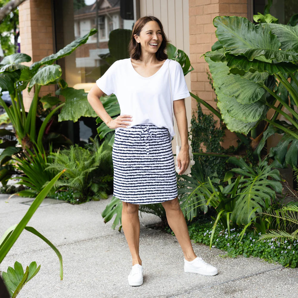 Brunette woman wearing a navy striped skirt and white top in a garden.
