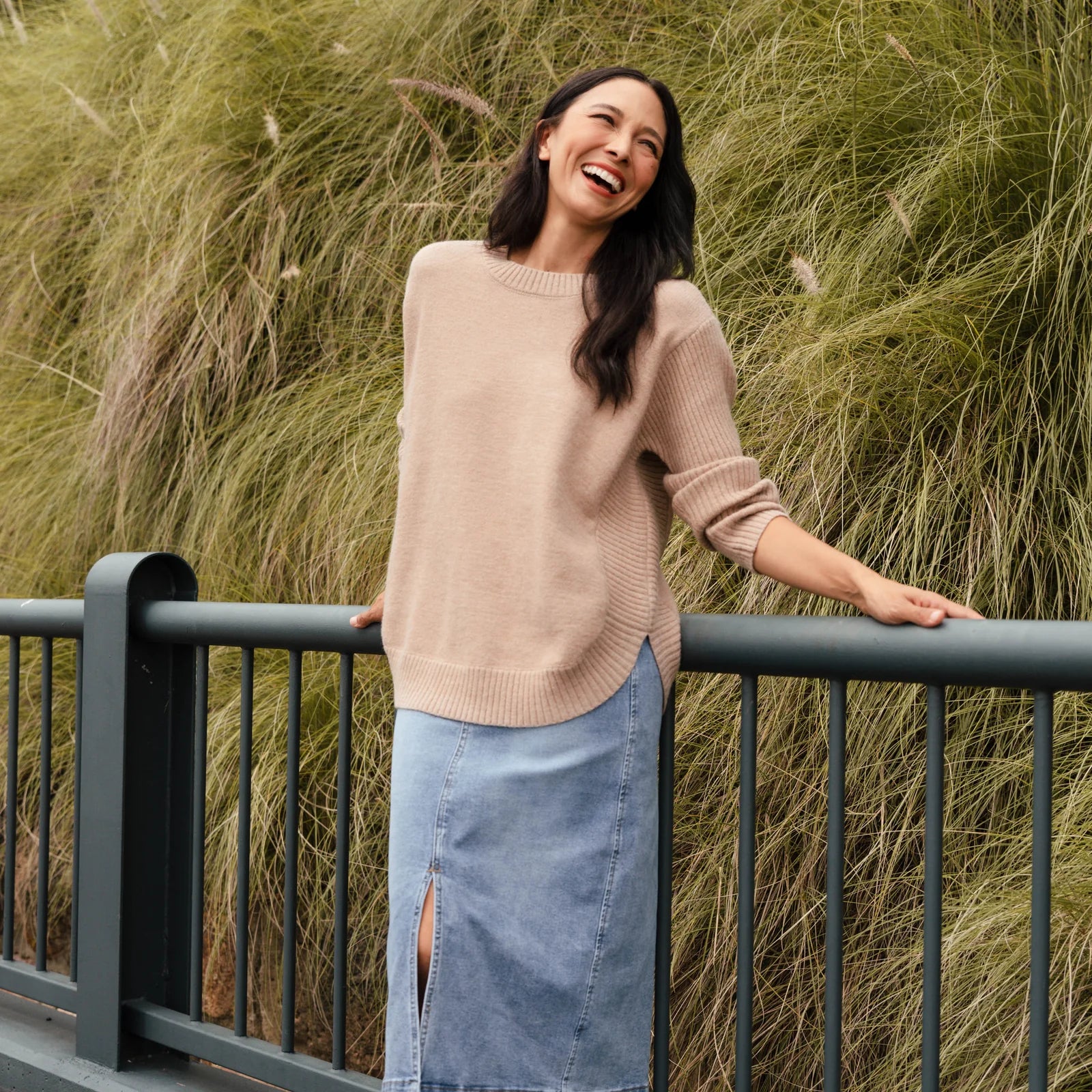 Brunette woman in a beige knit sweater and blue denim skirt.