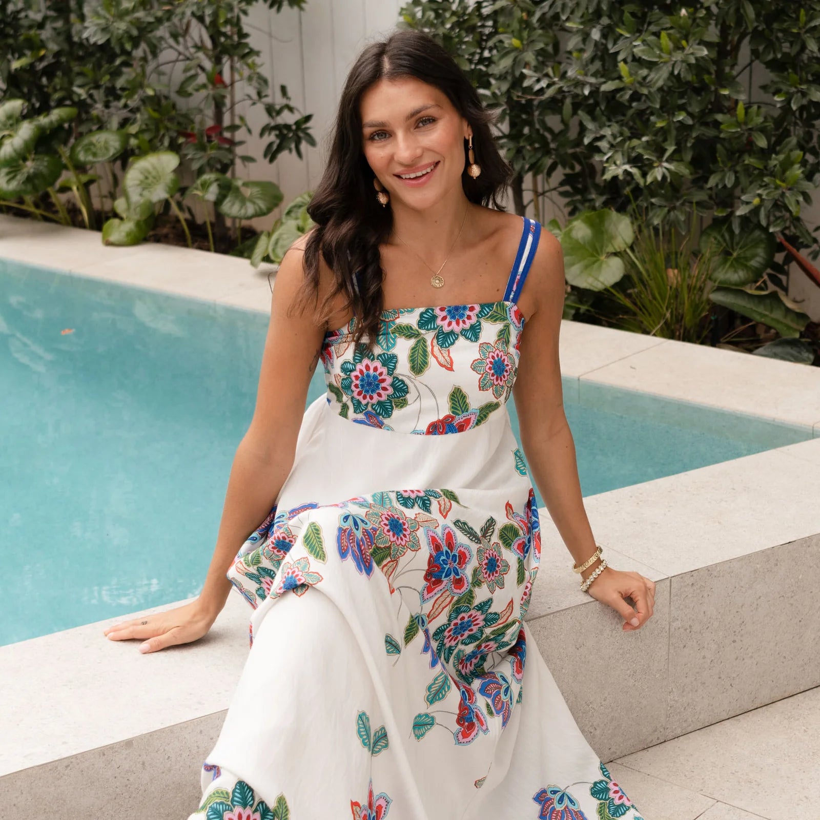Brunette woman wearing a floral dress beside a pool.