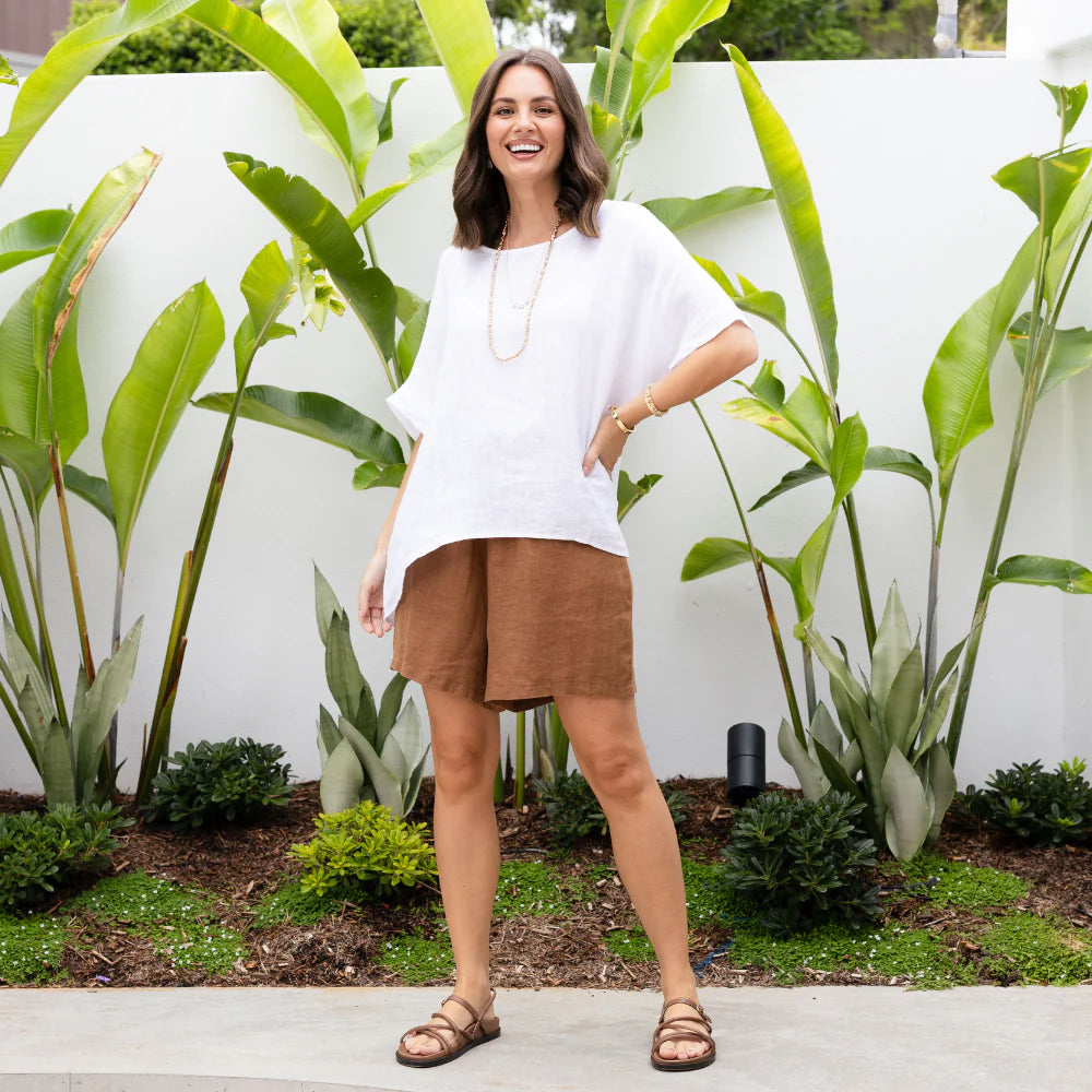 Brunette woman wearing a linen top and linen shorts in a tropical garden.