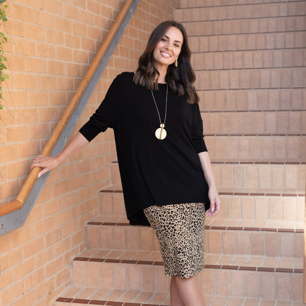 Brunette woman wearing a black jumper and leopard print midi skirt on brick stairs.