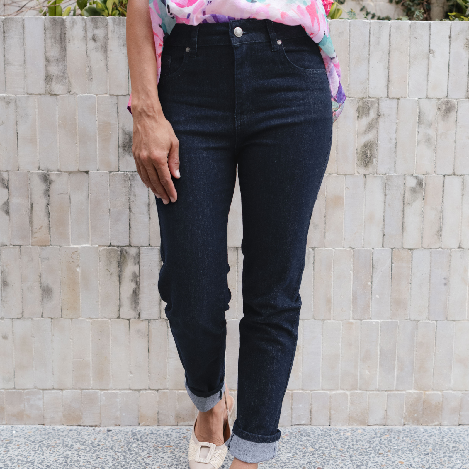 Woman wearing dark blue cuffed straight leg jeans in front of tiled wall.