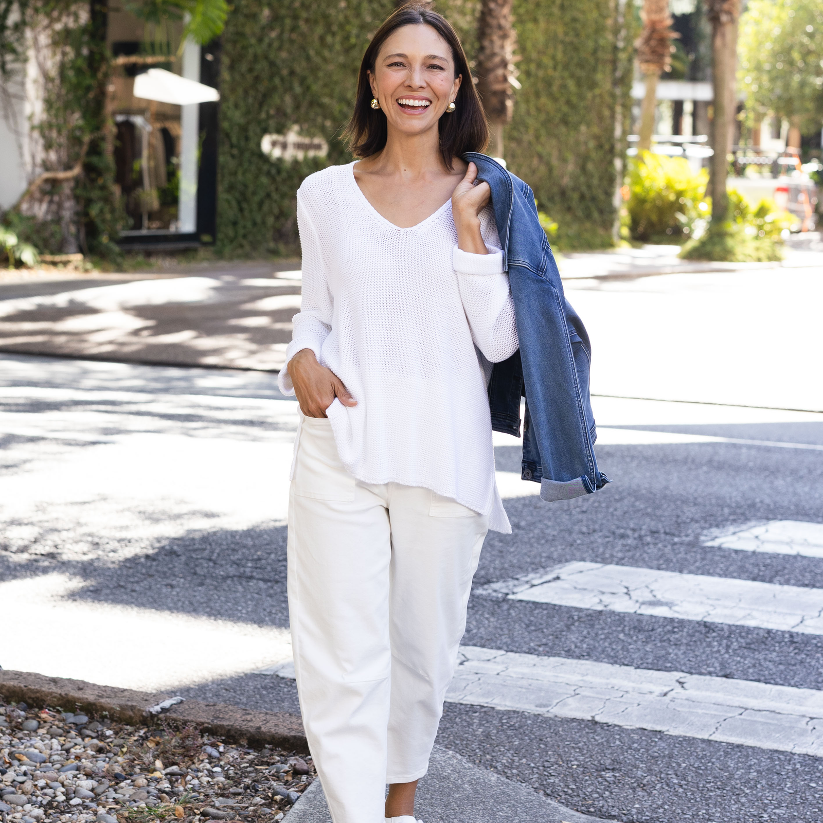 Brunette model with short hair wearing a white knit jumper and barrel jeans. 