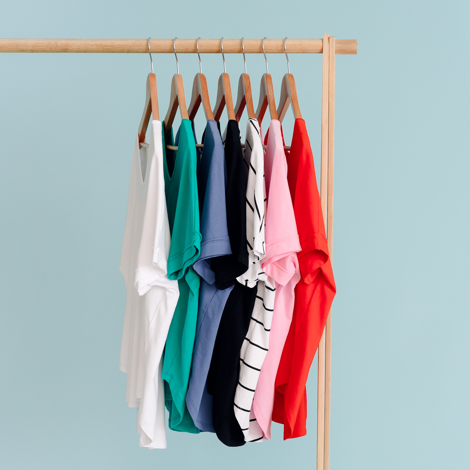 Colourful tees hanging up on a clothing rack.