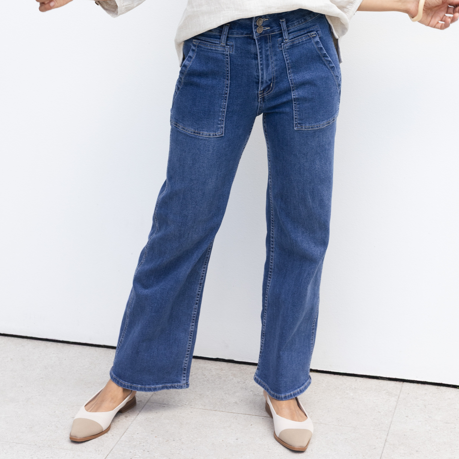 Woman wearing dark blue jeans in front of a white wall.